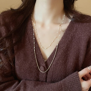 Detail of layered gold snake chain and pearl necklace worn on model neck