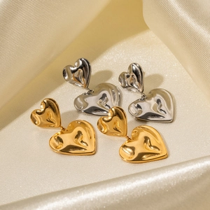 Textured gold and silver double heart drop earrings on beige satin fabric backdrop