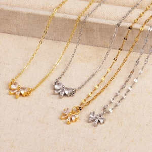 Détail de pendentifs nœuds dorés et argentés avec zircon sur un tissu beige texturé