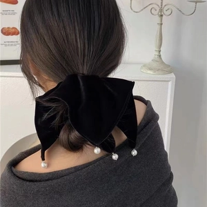Detail of black velvet bow hair tie with faux pearl pendants on a low bun hairstyle