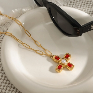 Détail du pendentif croix dorée avec pierres rouges et perle sur tissu texturé