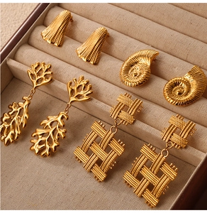Macro view of gold-plated seashell and geometric earrings on beige velvet display