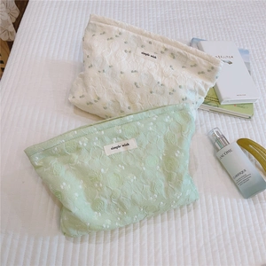Detail of mint green and pearl white jacquard makeup bags on white quilted bedding