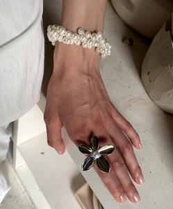 Close-up of a silver flower ring with a center pearl and layered pearl bracelet
