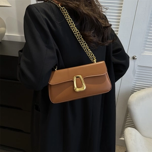 Brown leather baguette bag with gold chain strap shown on model in minimalist interior