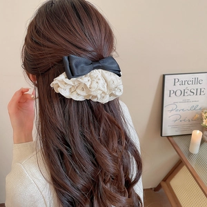 Détail d'un nœud en satin noir et dentelle blanche brodée sur cheveux bruns ondulés