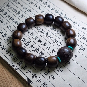 Détail de perles de bois avec perle centrale gravée et espaceurs turquoise sur calligraphie