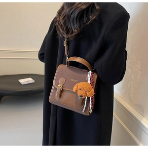 Brown vintage leather shoulder bag with plush dog charm worn by model in minimalist setting
