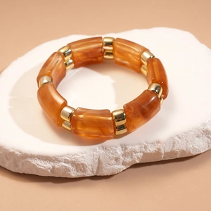 Detailed macro view of amber acrylic segments and gold metal beads on elastic bracelet