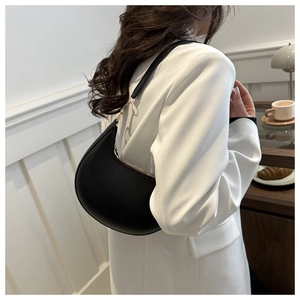 Elegant black crescent shoulder bag shown on shoulder of model in white suit