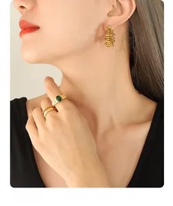Detail of gold geometric tiered hoop earrings and green gemstone ring on a model