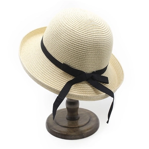 Detail of beige woven straw hat with black ribbon bow on a dark wood display stand