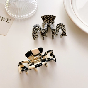Minimalist geometric hair claws in leopard print and checkered patterns on a cream surface