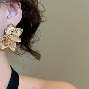 Macro shot of large golden petal earrings with layered metal texture on female model