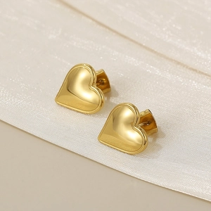 Macro shot of polished gold heart stud earrings on elegant pearlescent fabric background