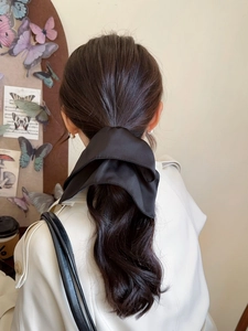 Detail of a glossy black satin bow hair tie worn on a ponytail with a silky drape effect