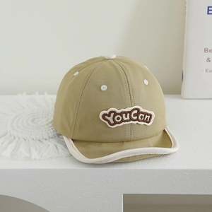 Close-up of khaki cotton baby hat with soft brim, white piping, and 'You Can' embroidery