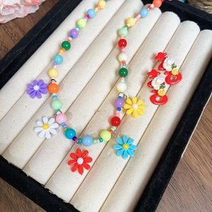 Detail of colorful beaded necklace with floral charms and festive red earrings in a box