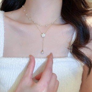 Close-up of double-layer gold necklace featuring pearl accents and a white camellia flower
