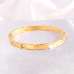 Detailed view of gold stainless steel bangle with clover motifs and sparkling crystals