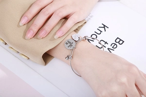 Detail of silver heart and mama pendant bracelet on woman wrist with refined finish