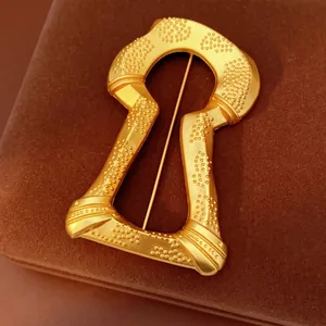 Vintage gold keyhole brooch with matte textured finish and raised dots on velvet box
