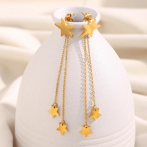 Close-up of gold star tassel earrings with long chains on a white ceramic vase