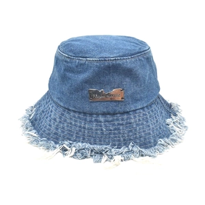 Detailed macro view of the distressed raw edges and silver metal plaque on denim bucket hat