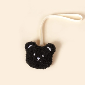 Gros plan d'une attache-tétine ours en peluche noire avec ruban crème sur fond jaune