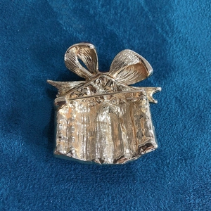 Close-up of golden metal gift box brooch with bow design showing detailed back structure