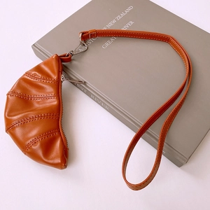 Detail of a brown faux leather croissant pouch necklace on a gray book background