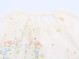 Détail de la broderie florale et de l'imprimé sur un chemisier en mousseline beige fluide