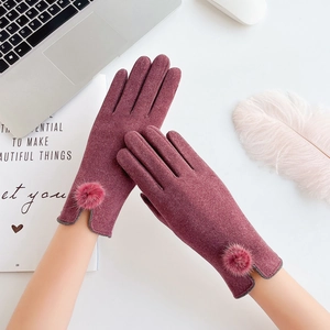 Detail of burgundy thermal gloves with faux fur pom-pom trim and touchscreen fingers