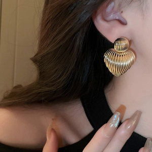 Detail of model wearing gold heart earrings with vintage pleated metal texture