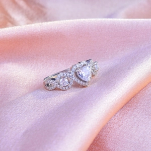 Elegant silver heart-shaped engagement ring with pavé diamonds on pink silk background