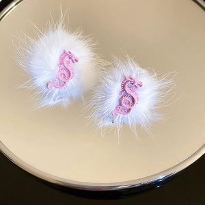 Detail of white plush earrings with pink dragon charms on a reflective mirror base