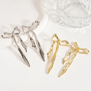 Boucles d'oreilles nœuds dorées et argentées avec texture métallique sur plateau blanc
