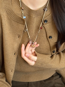 Detail of tiger eye horse pendant on pearl necklace worn over a brown cardigan sweater