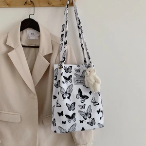 Close-up of white canvas tote with black butterfly prints and a cute plush bear charm