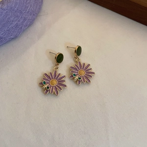 Close-up of golden daisy stud earrings with purple petals and green bee details