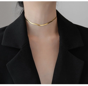 Detailed close-up of a minimalist flat gold snake chain necklace on a model