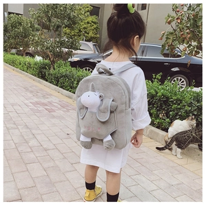 Outdoor shot of a grey plush kids backpack featuring a detachable white unicorn plush toy