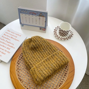 Detail of chunky ginger yellow knit beanie with rolled edge on a cozy rustic wooden tray