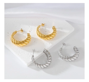 Detail view of gold and silver twisted C-shaped earrings on textured stone surface