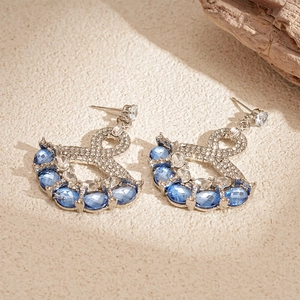 Detail of fan-shaped silver earrings with blue gemstones and zircons on a textured surface