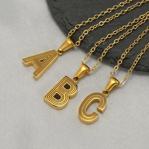 Three gold stainless steel letter necklaces A B and C with concentric texture on gray background