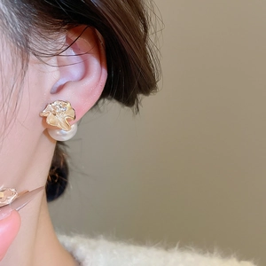 Macro shot of gold-plated floral stud earrings with large pearl drop on a model