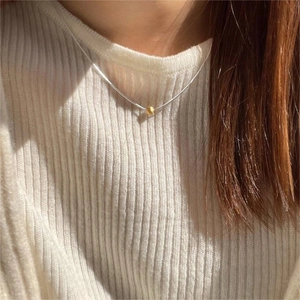 Detail of a gold bead pendant on a minimalist silver snake chain worn on the neck