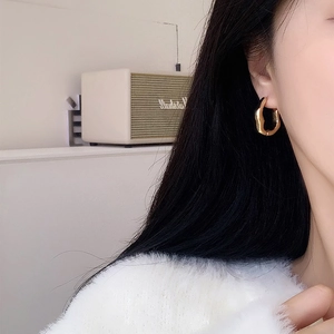 Close-up of model wearing irregular gold geometric hoop earrings with a metallic finish
