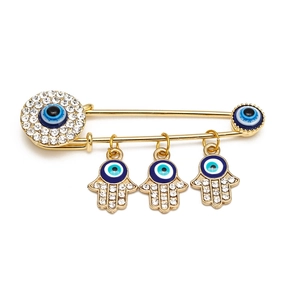 Detailed close-up of golden Evil Eye safety pin brooch with Hamsa Hand charms and crystals